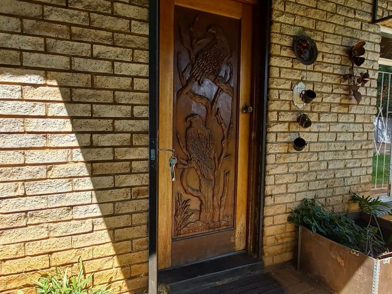 Entrance area featuring a distinctive carved wooden door set within a face brick facade, complemented by security-fitted windows and paved exterior flooring.