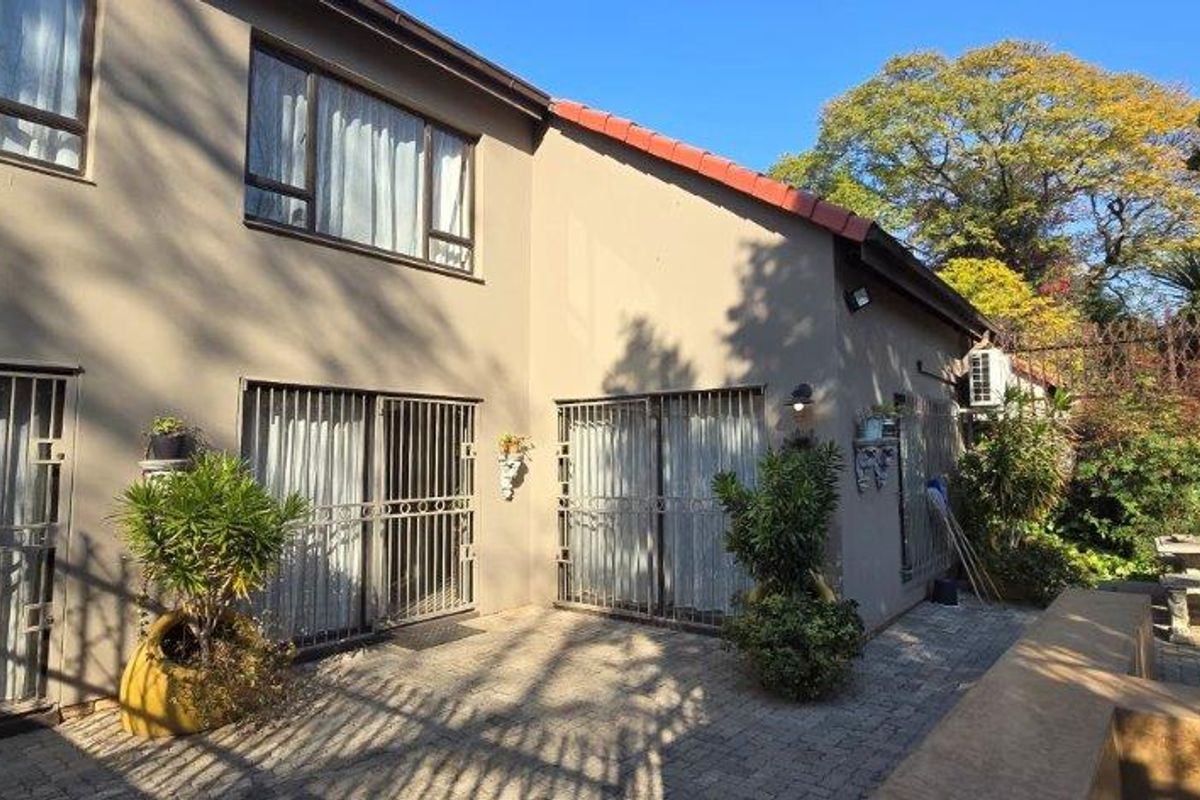 Rear exterior view of the townhouse featuring a paved patio area, sliding glass doors with security gates, and established garden surroundings.