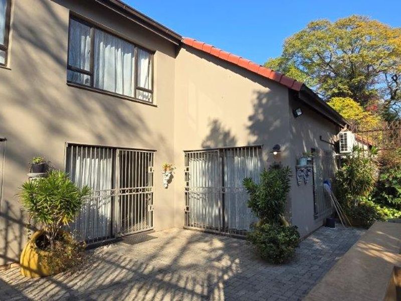 Rear exterior view of the townhouse featuring a paved patio area, sliding glass doors with security gates, and established garden surroundings.