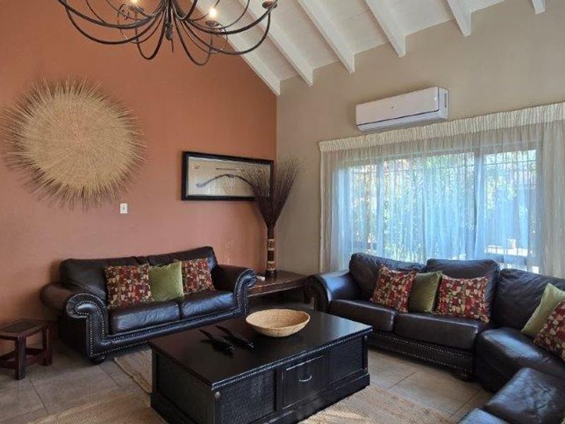 Spacious living room featuring a high vaulted ceiling with exposed rafters, tiled flooring, and a wall-mounted air conditioning unit.