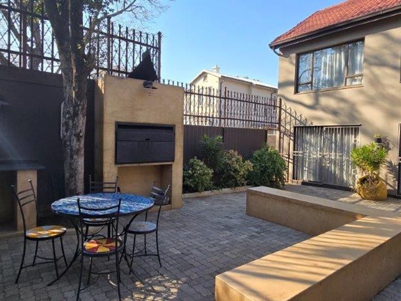 A paved outdoor patio area featuring a built-in braai, integrated seating, and secure perimeter fencing, providing a functional space for outdoor entertaining.