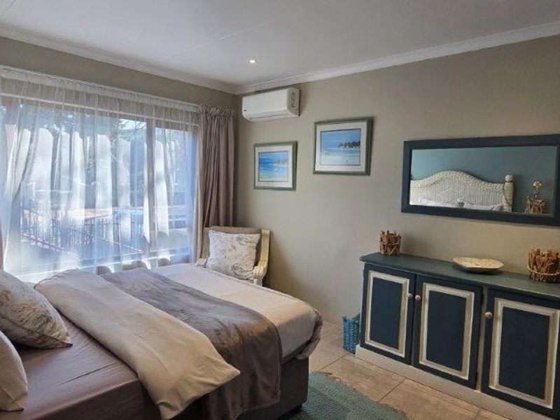 A comfortable bedroom featuring tiled flooring, a large window with curtains, and a wall-mounted split-system air conditioner for climate control.