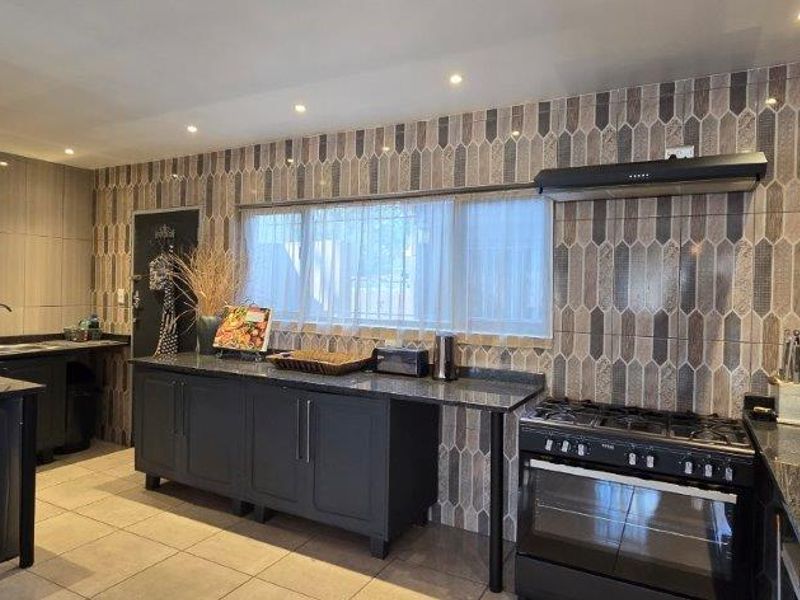 Modern kitchen featuring dark cabinetry, granite countertops, a gas stove with extractor fan, and decorative tiled backsplash with recessed lighting.