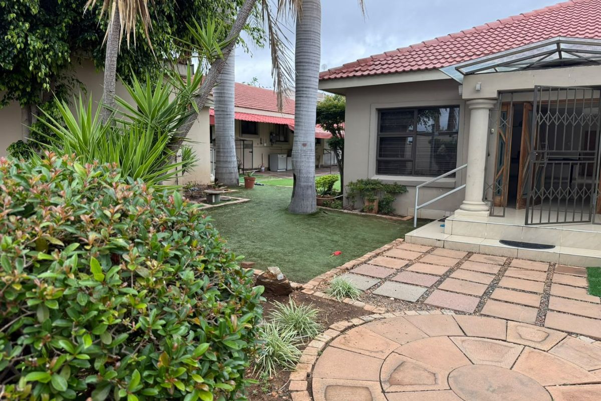A rear exterior view featuring a paved patio area, artificial lawn, and a covered entrance with security gate.