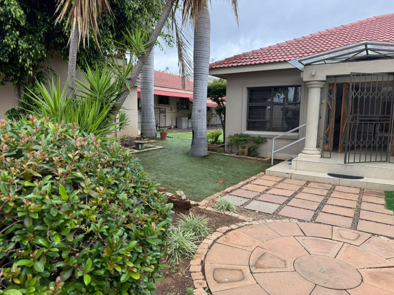 A rear exterior view featuring a paved patio area, artificial lawn, and a covered entrance with security gate.