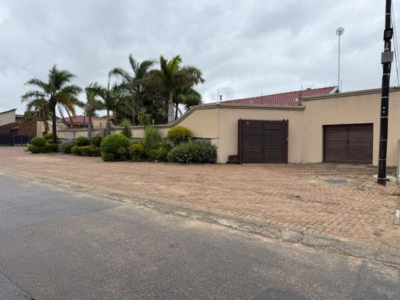 Front exterior view of the property featuring a paved driveway, boundary wall with electric fencing, and secure wooden garage and pedestrian access gates.