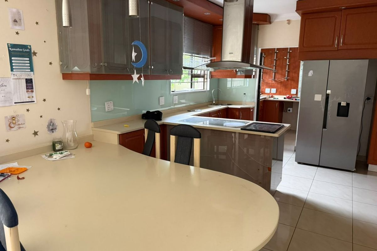 A functional kitchen featuring wood and grey cabinetry, stone countertops, a glass splashback, and a central breakfast bar area with tiled flooring.