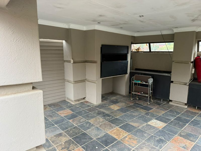 Covered patio area featuring slate tile flooring, a built-in braai, and integrated cabinetry, offering a functional outdoor entertainment space in need of minor cosmetic attention.