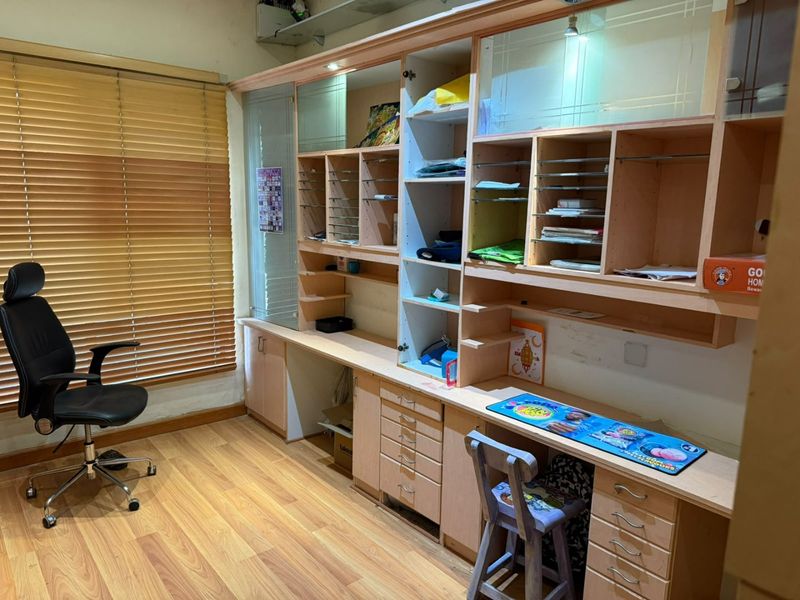 A dedicated home office featuring extensive built-in cabinetry, shelving, and a desk, complemented by laminate flooring and adjustable venetian blinds.
