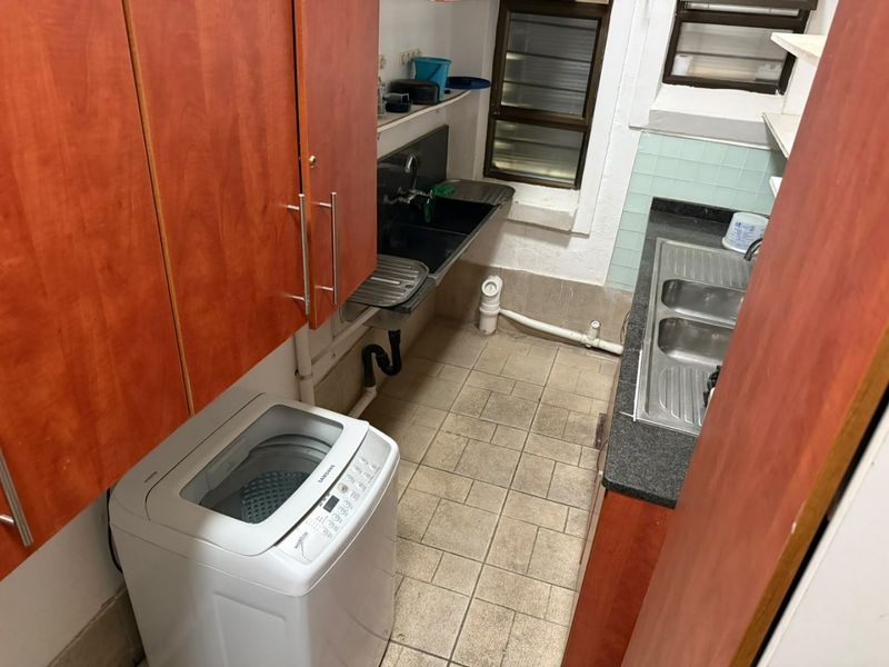 Functional scullery area featuring dual sink stations, laminate cabinetry, and tiled flooring, providing practical utility space for laundry and kitchen preparation.