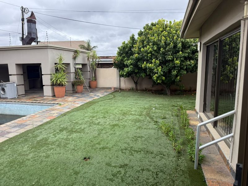 Outdoor pool area featuring a stone-paved patio, artificial lawn, and boundary wall with electric fencing, adjacent to the main house structure.