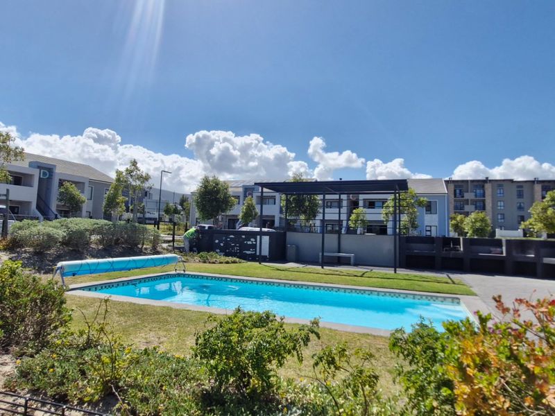 Communal pool area featuring a swimming pool with cover, a shaded pergola, and built-in braai facilities within a well-maintained apartment complex.