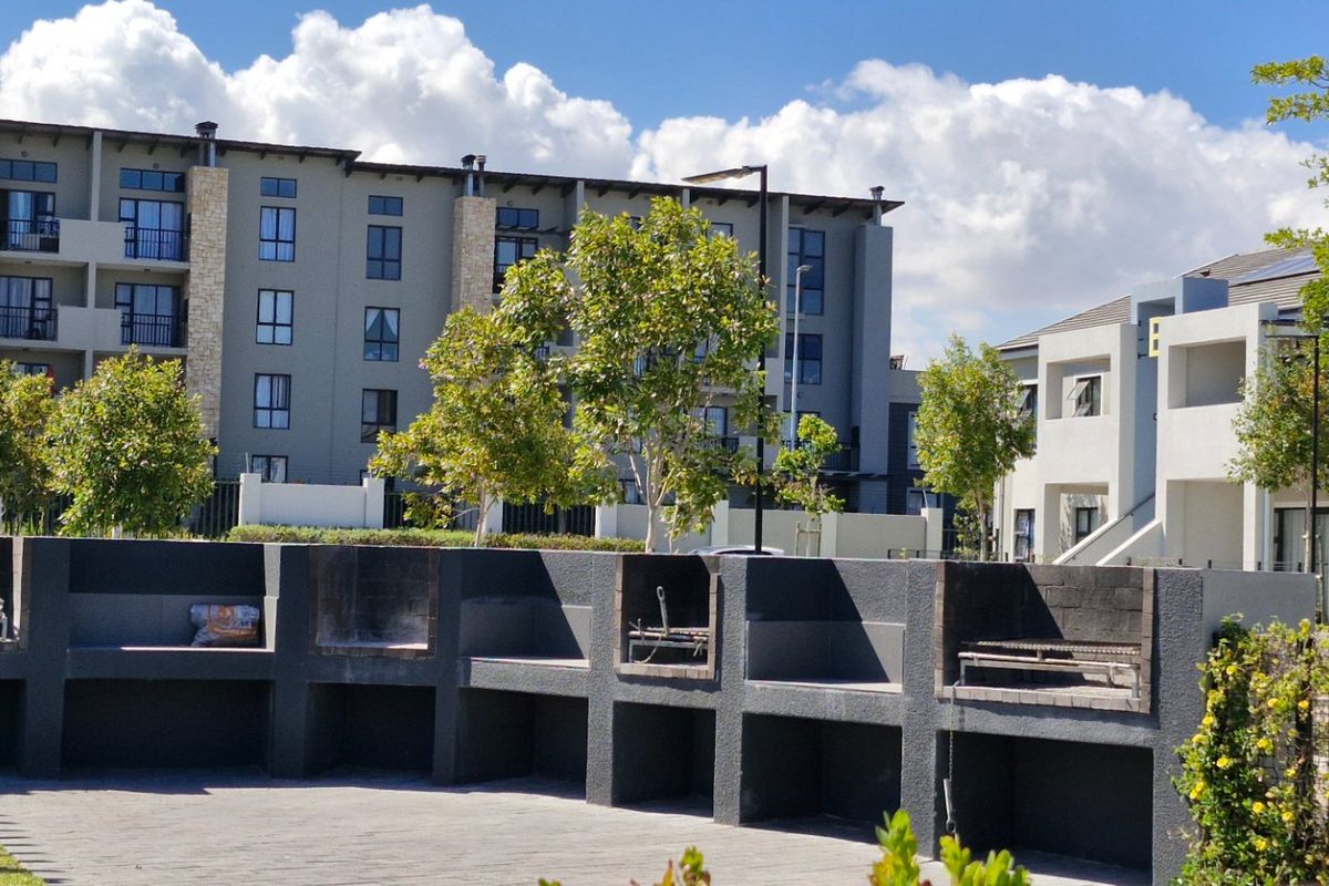 Communal outdoor area featuring multiple built-in braai stations set within a paved courtyard, surrounded by modern apartment complex buildings.