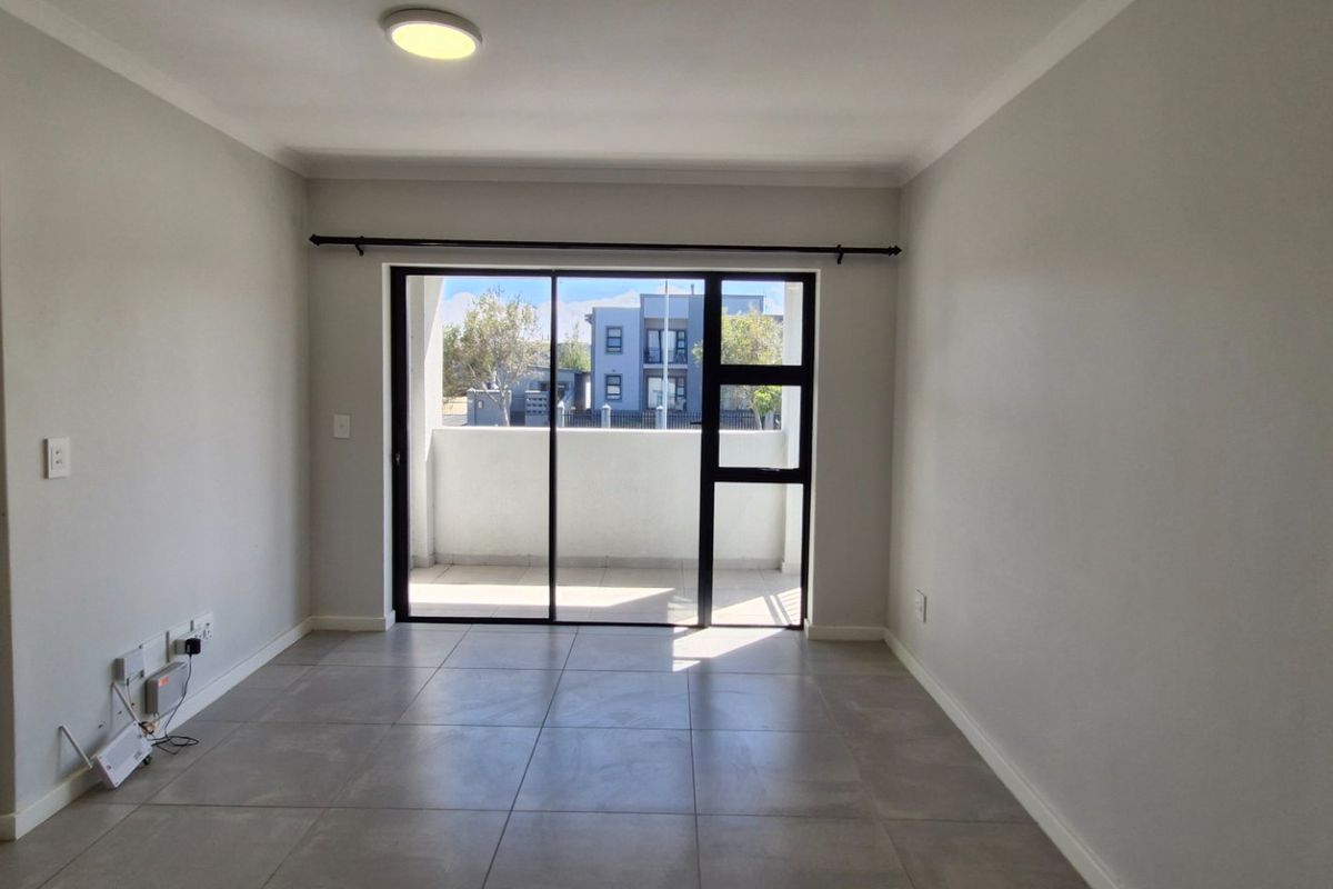 An empty, well-maintained living room featuring neutral tiled flooring, a modern ceiling light, and a large sliding glass door leading to a balcony.