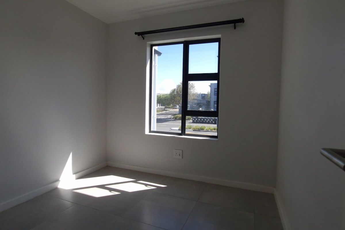 A bright, empty bedroom featuring neutral tiled flooring, clean white walls, and a modern aluminium window frame with a curtain rod.