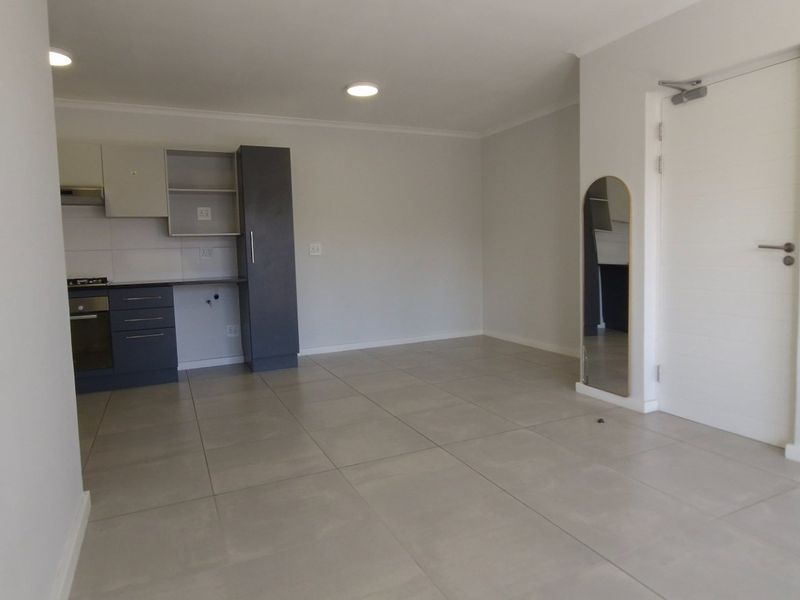 An open-plan living area featuring tiled flooring, recessed lighting, and a modern kitchen with built-in cabinetry, oven, and hob.