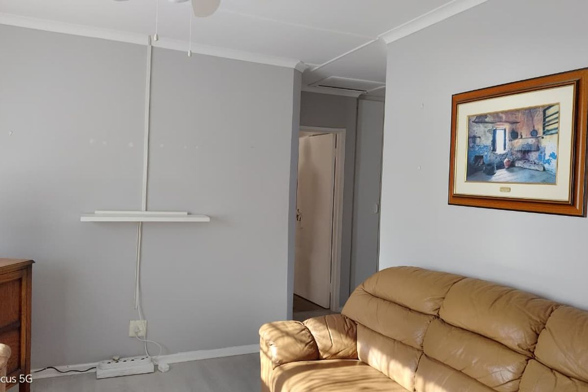 A living room area featuring laminate flooring, cove cornicing, and visible surface-mounted electrical conduit on the wall.
