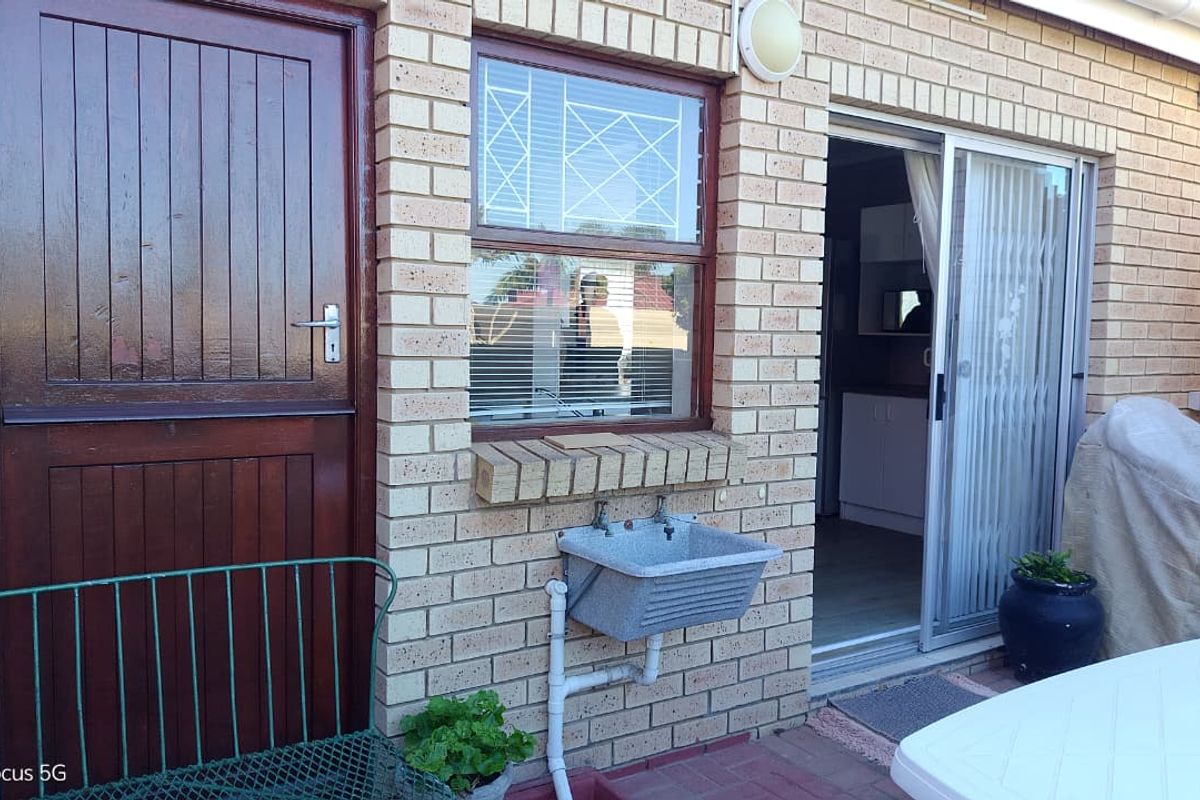 Rear exterior view of the townhouse featuring a face brick facade, a timber entrance door, a sliding glass door, and an external utility sink.
