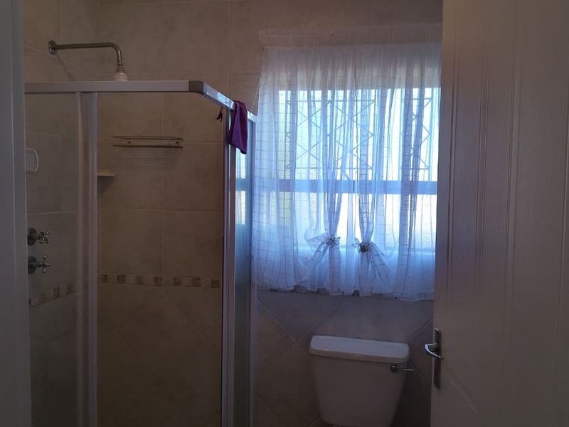 A functional bathroom featuring a shower enclosure, tiled walls, and a toilet, with natural light provided by a window with security bars.