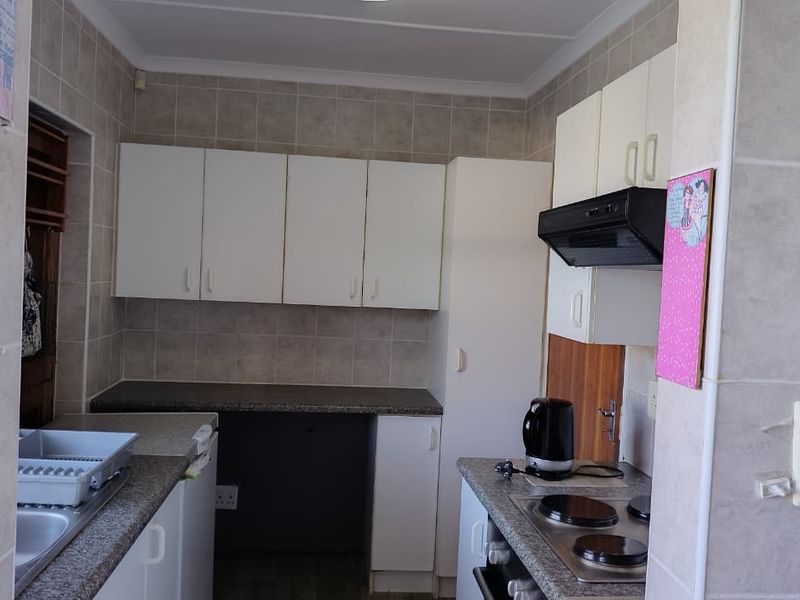 A functional kitchen featuring built-in cabinetry, laminate countertops, an electric hob with extractor fan, and tiled splashbacks.