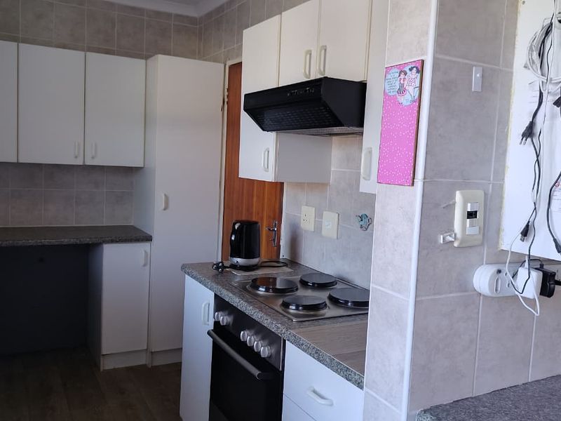 A functional kitchen featuring built-in cabinetry, an electric hob, oven, and extractor fan with tiled splashbacks and laminate countertops.