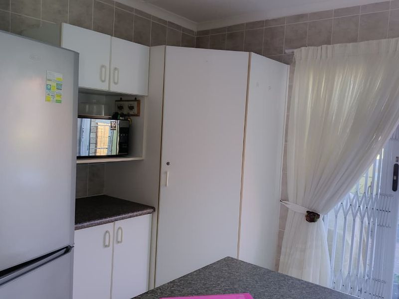 A functional kitchen area featuring white built-in cabinetry, laminate countertops, and a tiled backsplash, with direct access to an outdoor patio area.