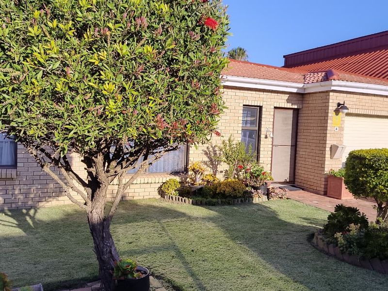 Front view of a face brick townhouse featuring a tiled roof, integrated garage, and a well-maintained front garden with paved access.