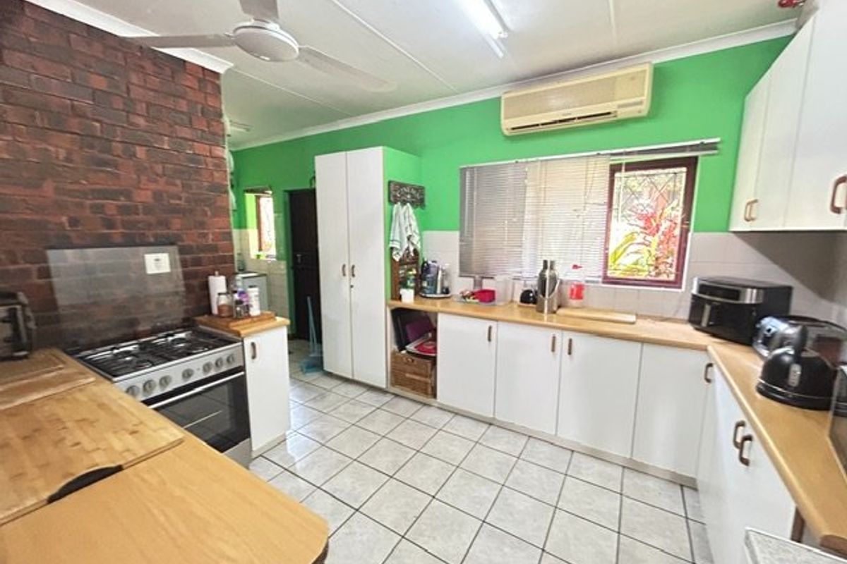 A functional kitchen featuring tiled flooring, white cabinetry, a gas stove, and an exposed brick feature wall, equipped with a ceiling fan and air conditioning.