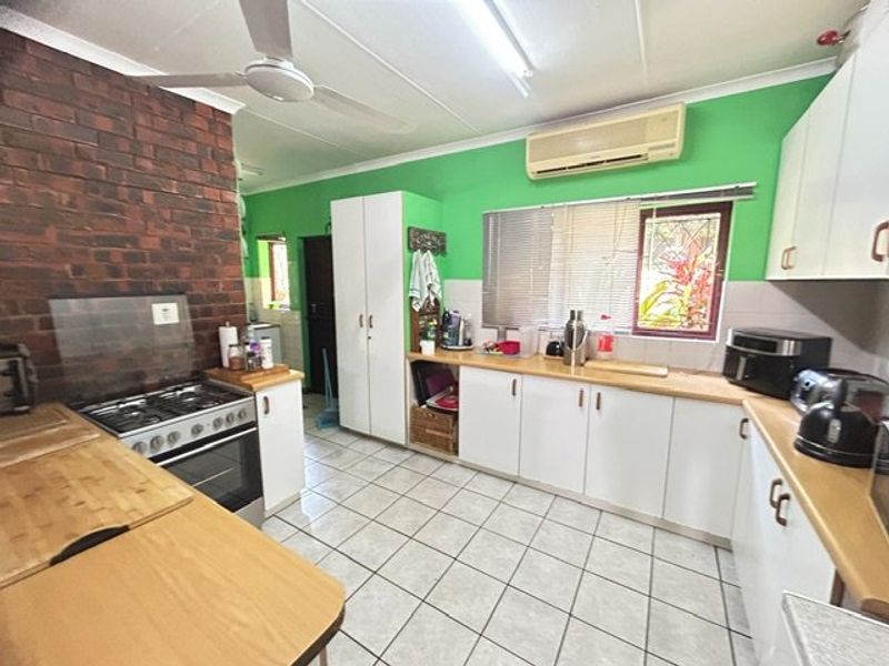 A functional kitchen featuring tiled flooring, white cabinetry, a gas stove, and an exposed brick feature wall, equipped with a ceiling fan and air conditioning.