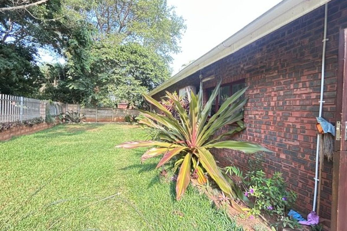 A view of the rear exterior of the house featuring a brick facade, lawn, and boundary wall.
