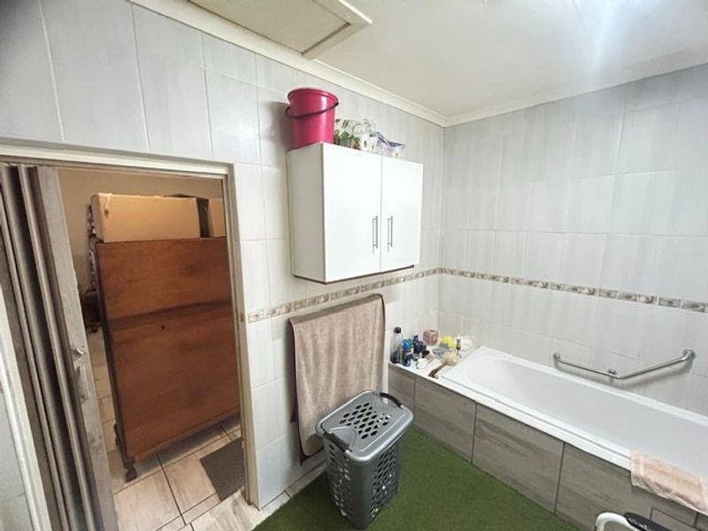 A functional bathroom featuring a bathtub with a grab rail, wall-mounted storage cabinetry, and full-height wall tiling.