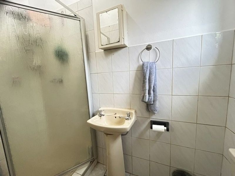 A dated bathroom featuring a pedestal basin, shower enclosure, and wall-mounted medicine cabinet with tiled wall finishes.