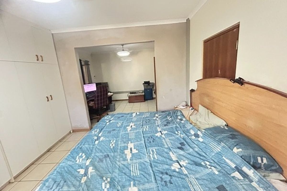 Bedroom featuring built-in cupboards, tiled flooring, and a ceiling fan, with an adjoining space visible through the doorway.
