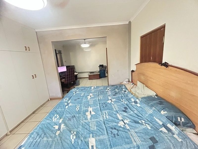 Bedroom featuring built-in cupboards, tiled flooring, and a ceiling fan, with an adjoining space visible through the doorway.