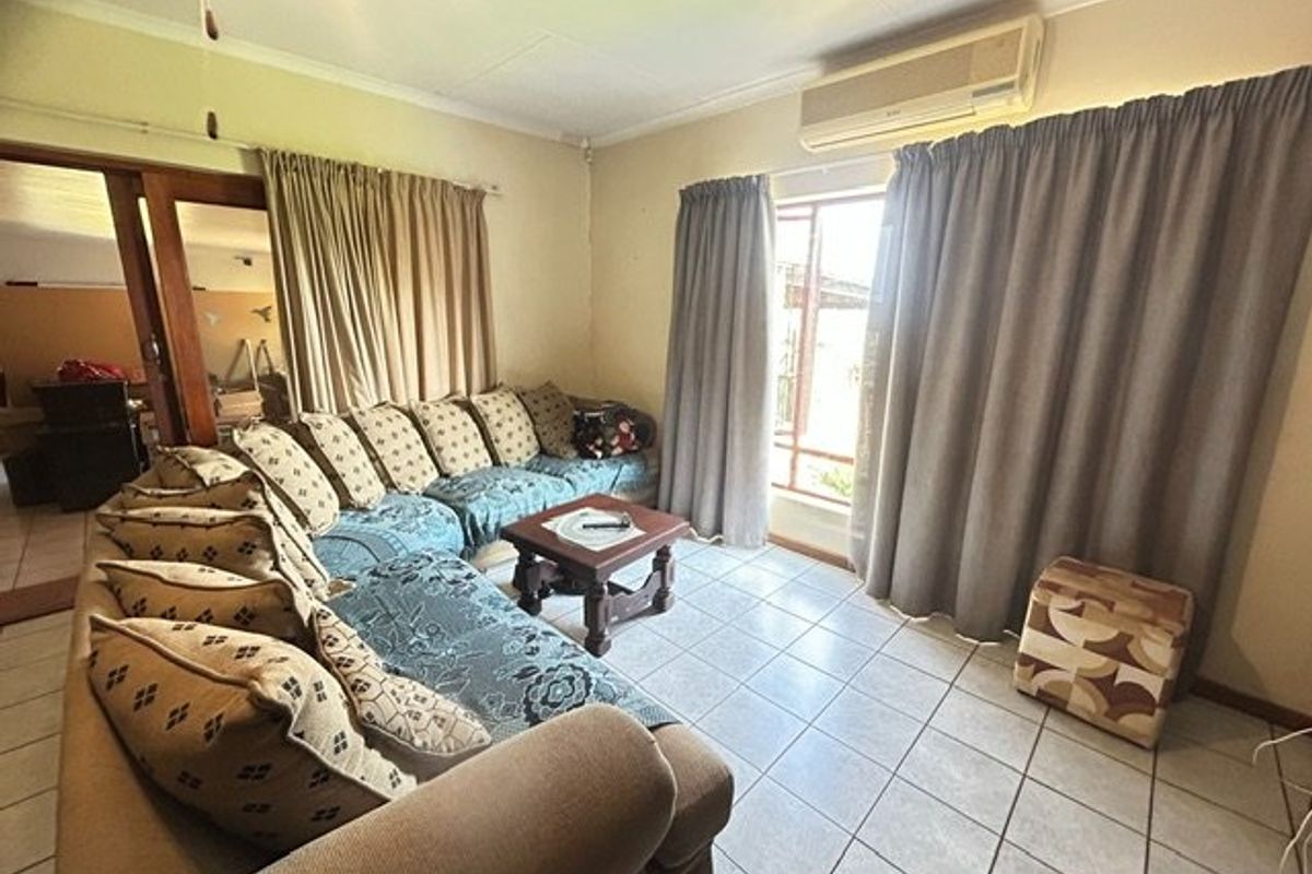 A living room featuring tiled flooring, a wall-mounted air conditioning unit, and access to an adjoining space through a sliding door.