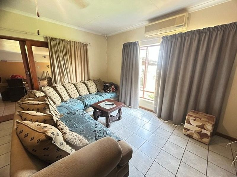 A living room featuring tiled flooring, a wall-mounted air conditioning unit, and access to an adjoining space through a sliding door.