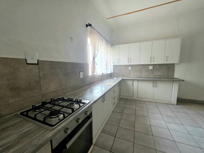 A functional kitchen featuring white cabinetry, laminate countertops, a gas hob, built-in oven, and neutral tiled flooring with a tiled backsplash.