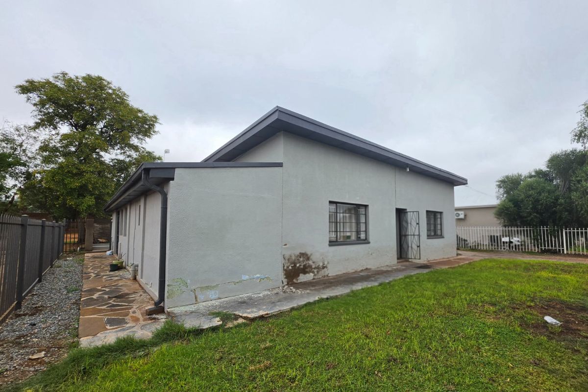 Rear view of the house featuring a stone paved walkway, metal security bars on windows, and a grassed garden area.
