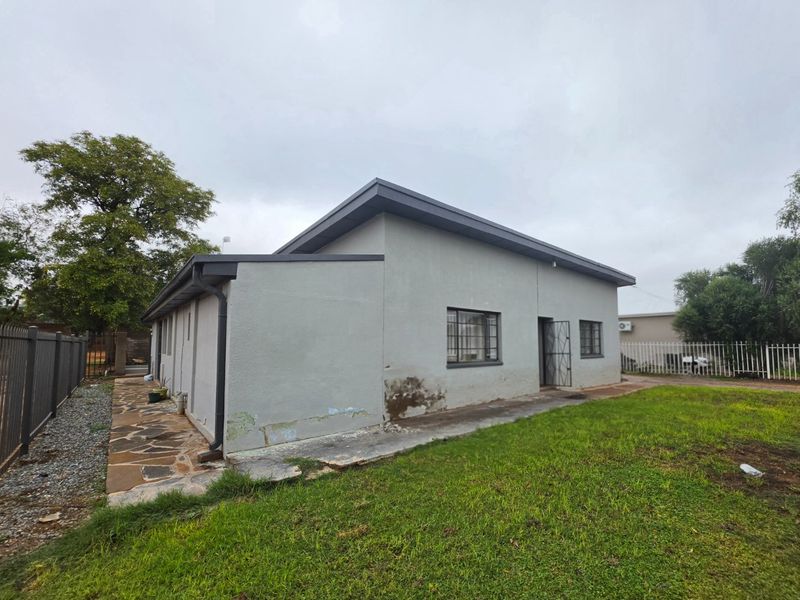 Rear view of the house featuring a stone paved walkway, metal security bars on windows, and a grassed garden area.