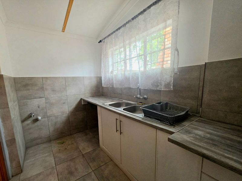 A functional laundry area featuring a double stainless steel sink, tiled splashbacks, and built-in cabinetry with ample counter space.