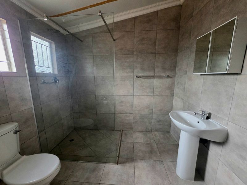 Modern bathroom featuring a walk-in shower with glass screen, pedestal basin, toilet, and neutral floor-to-ceiling tiling.