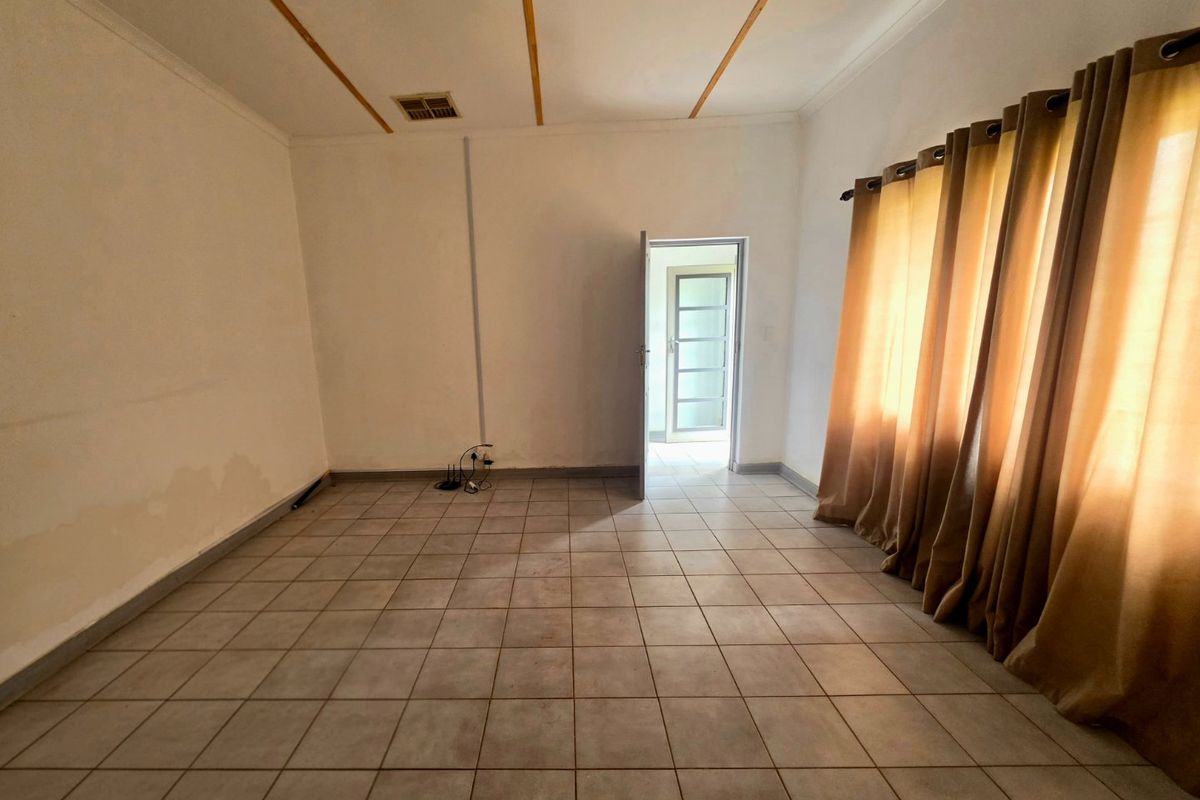 An empty living room featuring tiled flooring, neutral walls, and natural light through large windows.