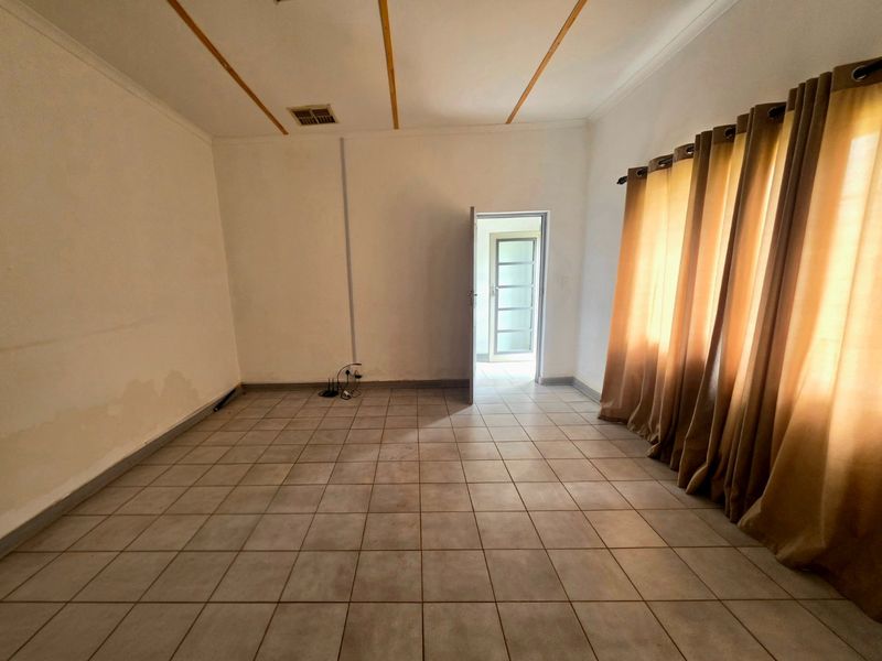 An empty living room featuring tiled flooring, neutral walls, and natural light through large windows.