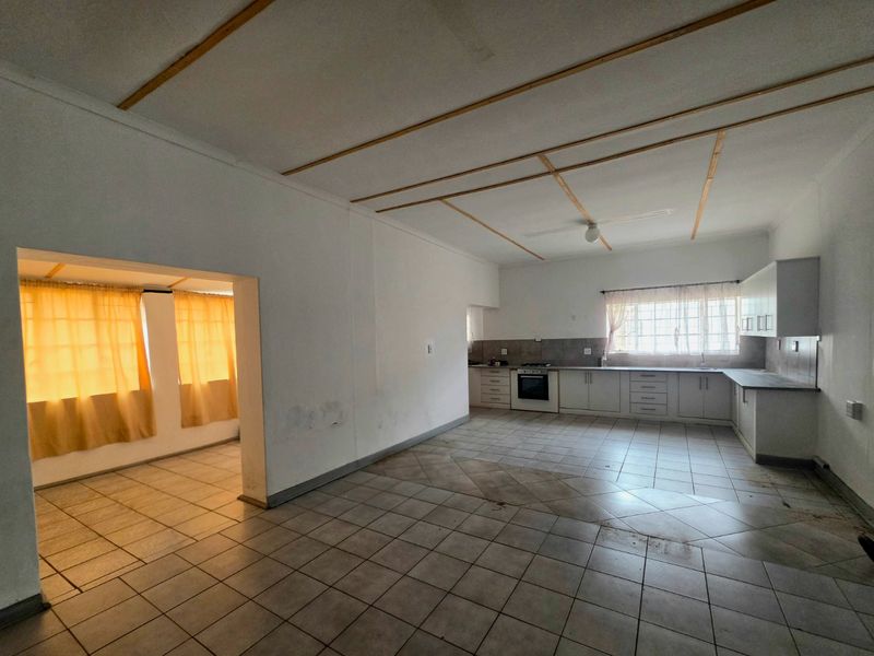 Spacious open-plan kitchen and living area featuring tiled flooring, built-in cabinetry, and integrated cooking appliances, offering a blank canvas for renovation.
