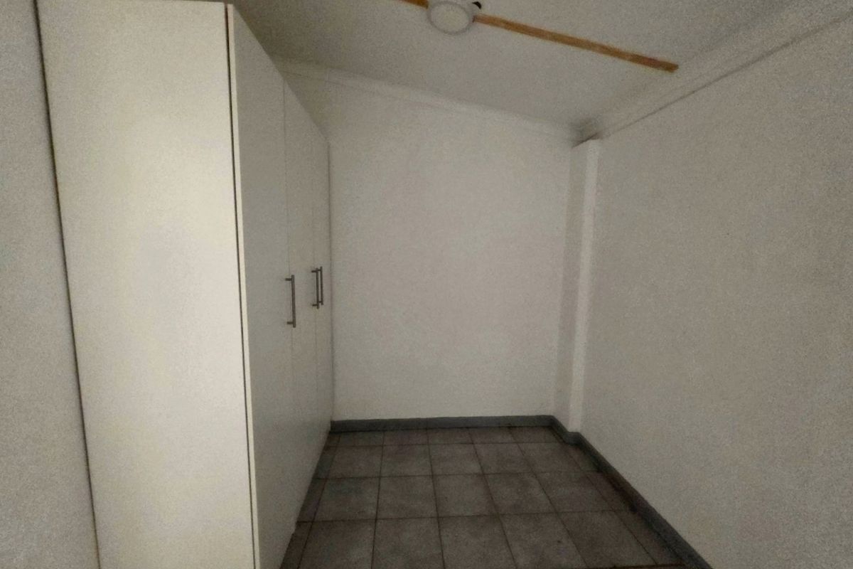 A compact, empty bedroom featuring tiled flooring and a built-in wardrobe, offering a neutral space ready for personalization.