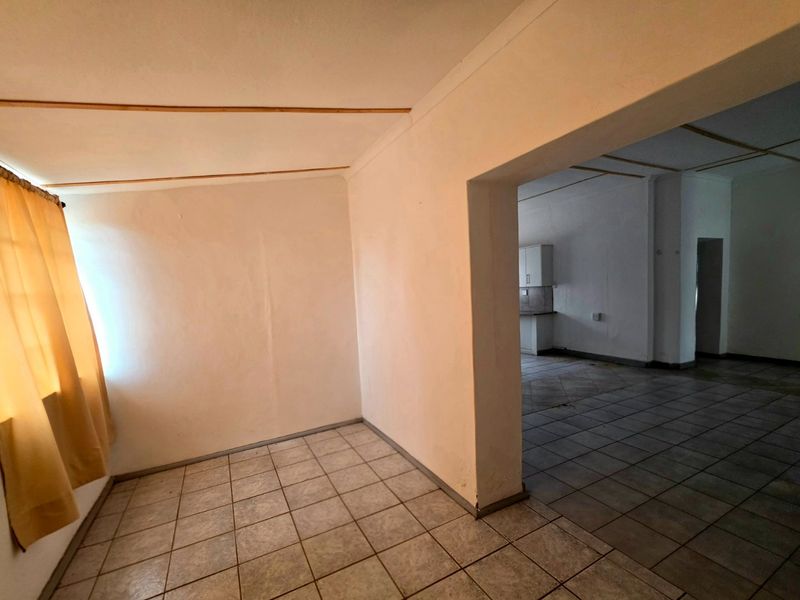 An open-plan living and kitchen area featuring ceramic floor tiles and a coved ceiling, offering a blank canvas for renovation and modernization.