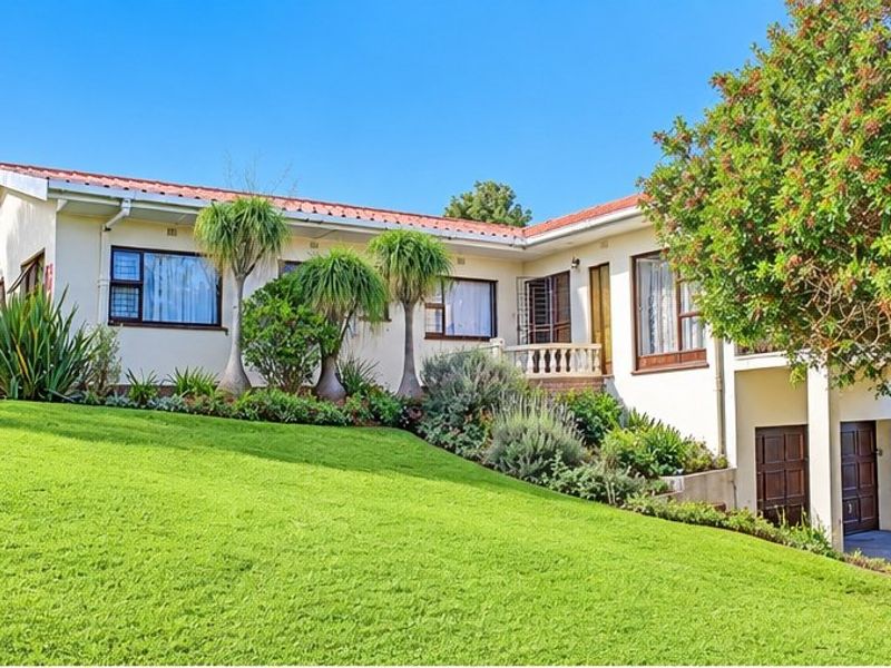 A well-maintained single-story residence featuring a tiled roof, established garden, and integrated garage, set on a sloping lawn.