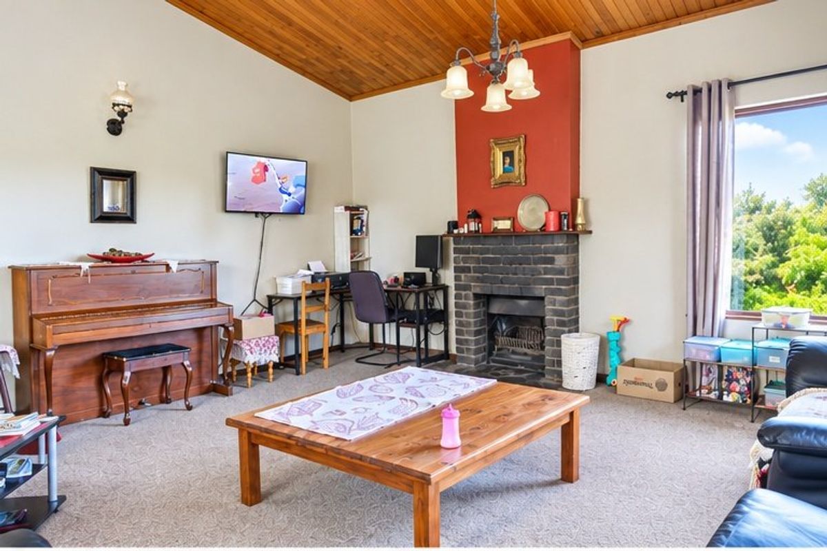 Spacious living room featuring a brick fireplace, vaulted timber-lined ceiling, and large window providing natural light.