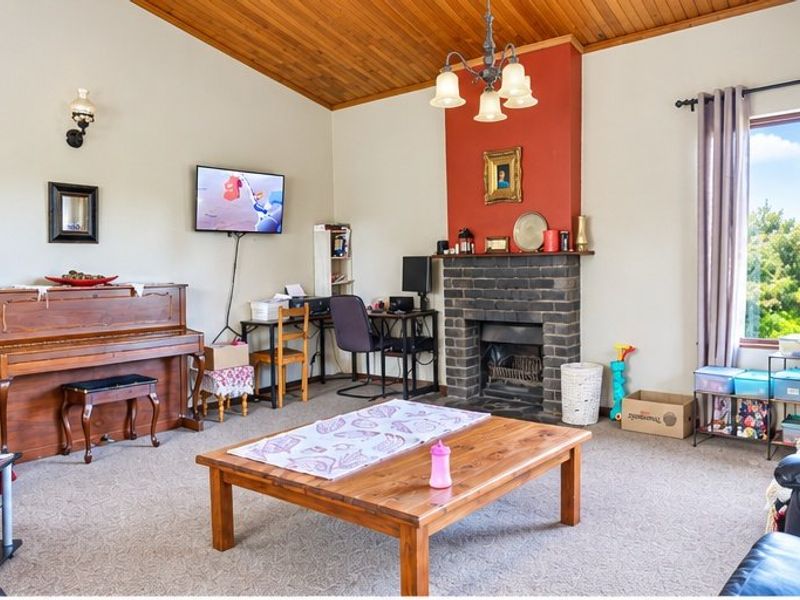 Spacious living room featuring a brick fireplace, vaulted timber-lined ceiling, and large window providing natural light.