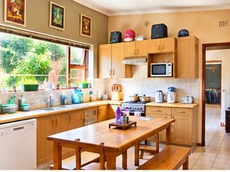 A functional kitchen featuring light wood cabinetry, laminate countertops, a tiled backsplash, and a large window overlooking the garden.